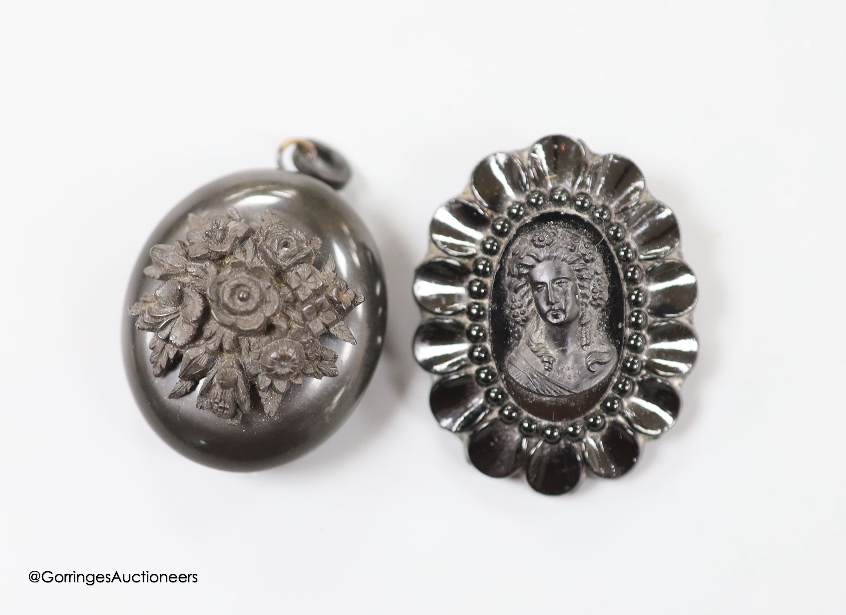 A jet oval pendant, carved with a bunch of flowers, 41mm and a similar brooch, carved with the bust of a lady.